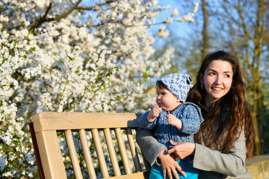 蹒跚学步的孩子和妈在开花的树背景上妈手上的小宝女人在盛开的春天花园里和孩子玩耍两个人的家庭的肖像幸福的家庭观念春天风景背图片