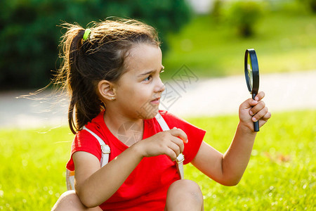 小女孩在绿公园玩放大玻璃游背景图片