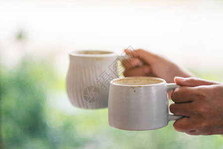 握着两杯白色咖啡热咖啡的双手和模糊自然背景图片