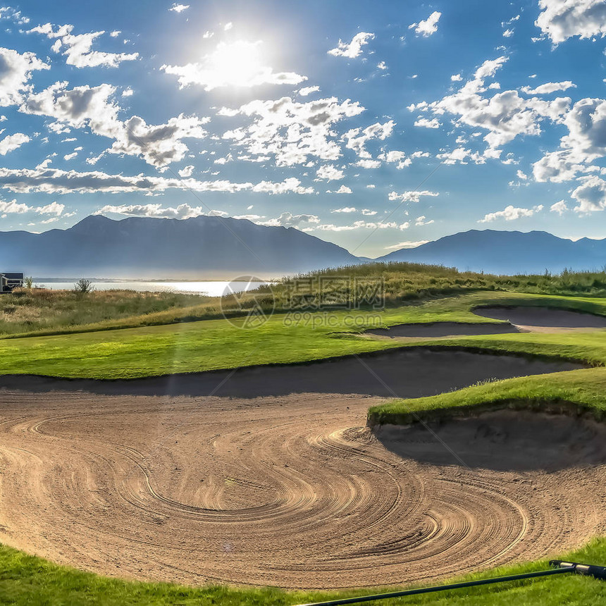 高尔夫球场的方形沙坑和天空中明亮的阳光和浮云的景色在风景优美的背景中可以看到房屋图片