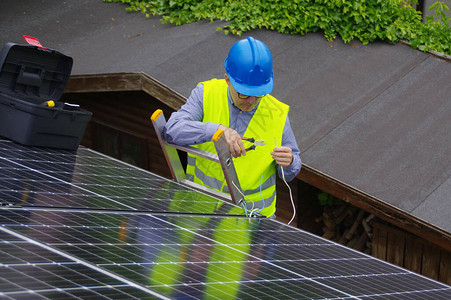 太阳能电池板的安装和调试私人住宅中的可再生能源梯子上的工人图片