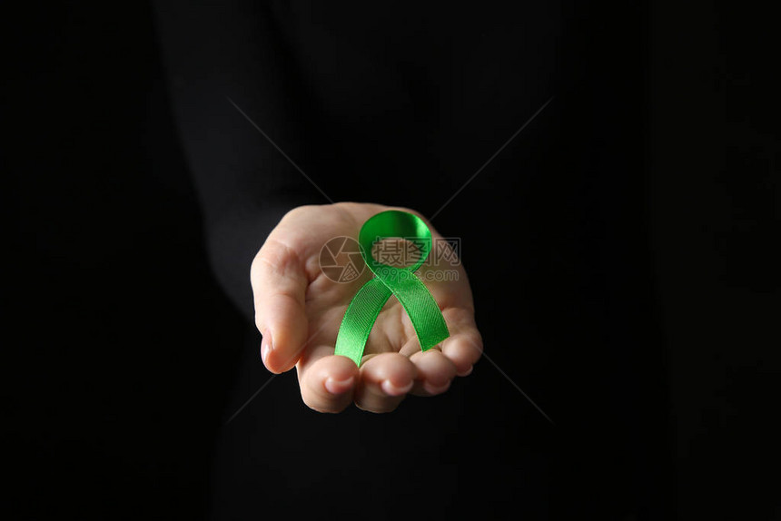 深色背景上带绿丝带的女手癌症意识概念图片