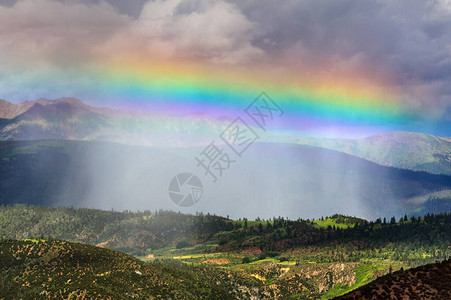 暴风雨阳光和直线彩虹笼罩在山上的一片绿山谷上图片