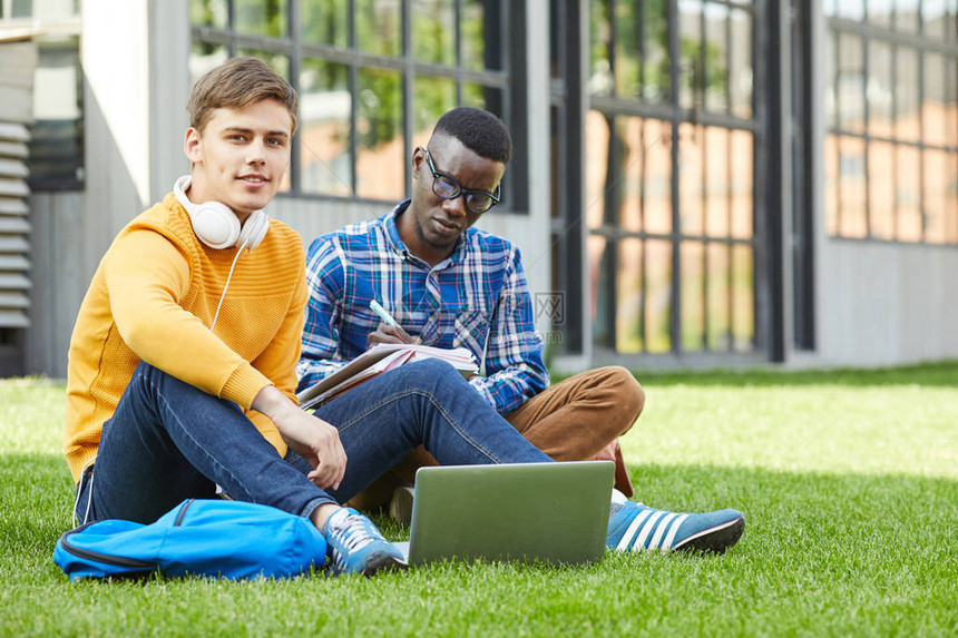 两名大学生坐在校园绿草上全长的肖像图片