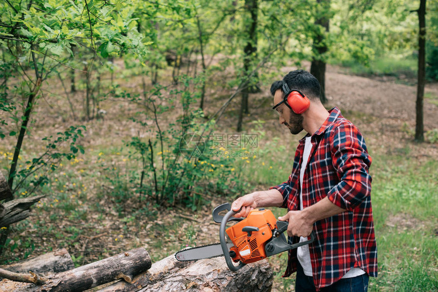 身穿格子衬衣和听力保护者用木锯砍林木的成年图片