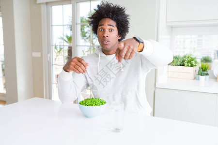 在家吃新鲜绿豌豆的非洲裔美国人用手指着相机和你图片