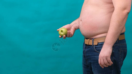 大肚子的胖子手里拿着一个青苹果健康饮食和减肥图片