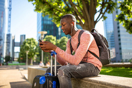 青年旅行男子与手机和手提箱一起坐在外图片