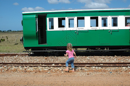 一个金发的白人女孩坐在铁轨上看着一辆绿色火车冒图片