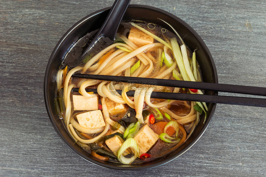 日本素食汤面条豆腐和蔬菜黑碗里有勺子和筷子顶图片