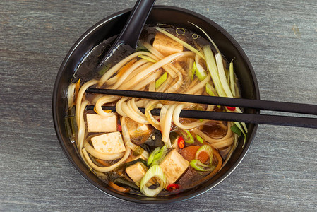 日本素食汤面条豆腐和蔬菜黑碗里有勺子和筷子顶图片