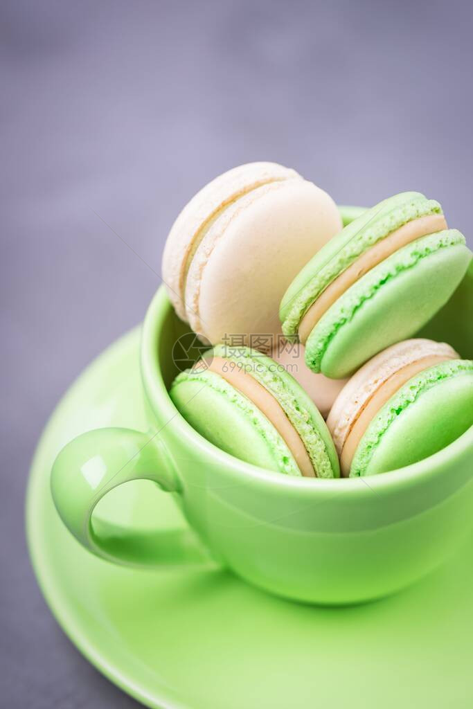自制法式马卡龙或马卡龙带饼干的绿色杯子灰色背景上带有香草奶油的薄荷饼图片
