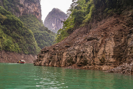 大宁河上的迷你三峡的舢板在翡翠绿的水面上绕着棕色悬崖岩石峡谷的弯曲航行一些绿色的树叶和银图片
