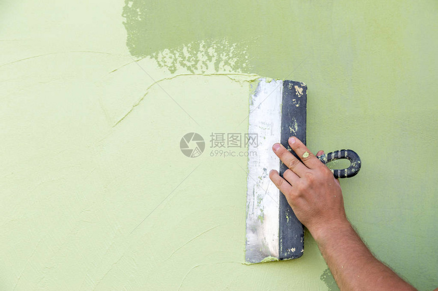 工匠手不带一根手指握着石膏和涂在绿色混凝土上的石膏的弹片图片