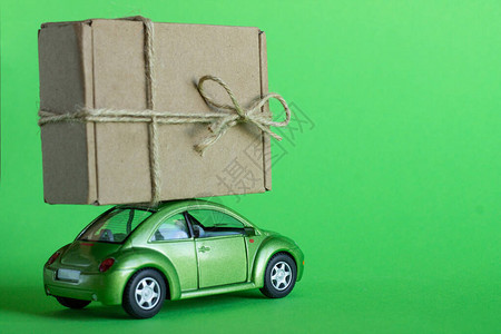 绿色玩具车在柔和的绿色背景上用工艺纸板箱运送包裹交付货物礼图片
