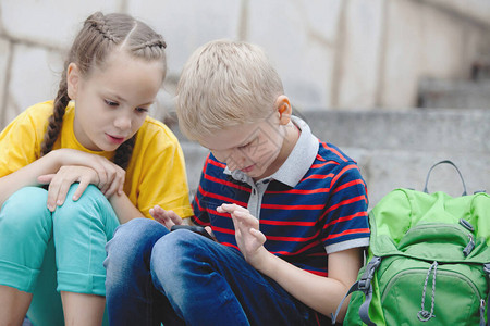 一个女孩有马尾和金发男孩看智能手机图片