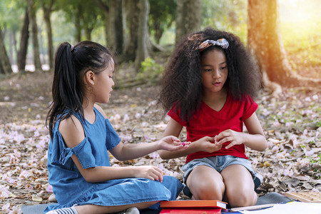 快乐的两个小女孩拿着橡皮泥在公园里坐在一起看东西与亚洲朋友一起玩时手里拿着橡皮泥的混血小学生背景图片