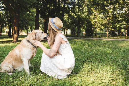 穿着白裙子和草帽的女孩在坐草地上时抚图片