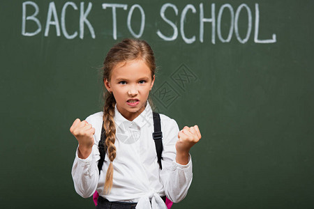 有选择的焦点愤怒的女学生看着镜头在粉笔板附近展示紧握拳头图片