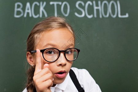 眼镜上可爱女学生的选择焦点在黑板附近展示思想姿态背回学校文字中图片