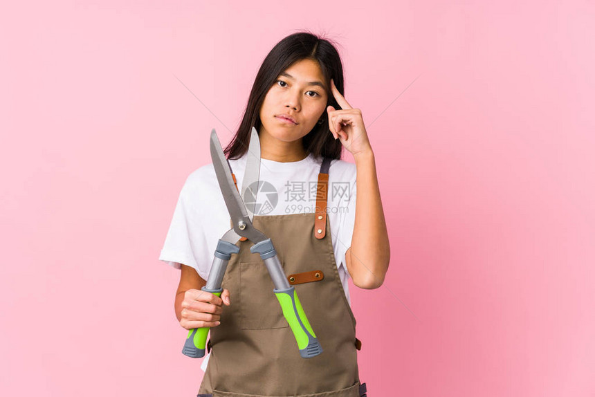 年轻的园丁女人拿着一把剪刀与世隔绝地用手指对着思考着专图片
