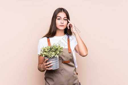 年轻的园丁caucasian年轻女人拿着一个植物隔离的用手指图片