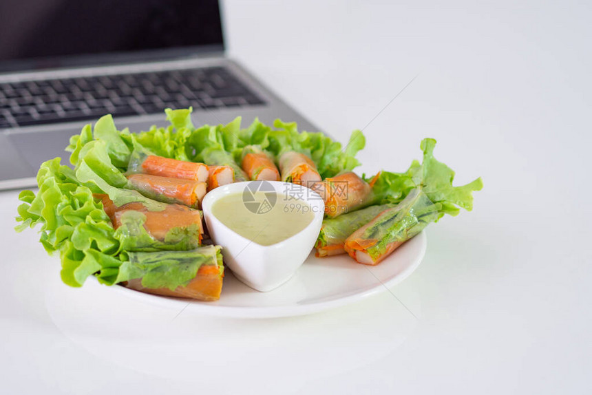 面条中的螃蟹棒和蔬菜沙拉以及桌上笔记本电脑附近的白碗上的酱汁图片