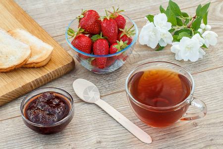 一杯茶自制草莓果酱木板上的面包和木本底的鲜草莓勺子和白茉莉图片