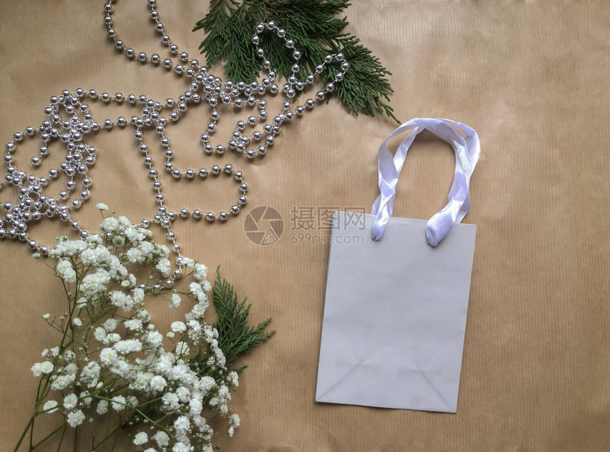 在浅褐色纸面背景灰纸礼品袋吉普西拉白色小花朵和带有银珍珠的圆柱形树枝上图片