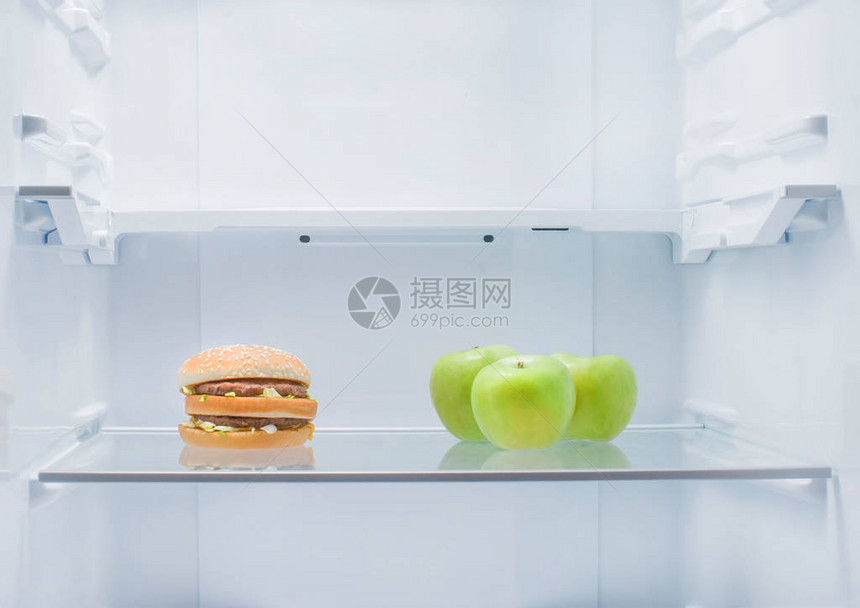 空冰箱里放着一个汉堡包和对面的新鲜青苹果健康食品和垃圾食图片