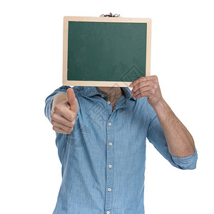 穿戴尼姆衬衣的年轻人用黑板蒙面做拇指印牌站在白色背景上孤图片