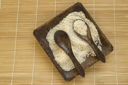 方形木盘上的生白米和竹餐巾上的两把木勺米饭图片