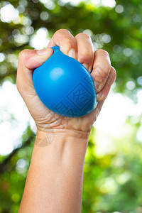 左手挤压蓝色压力球的女左手在bokeh绿色花园背景运动图片