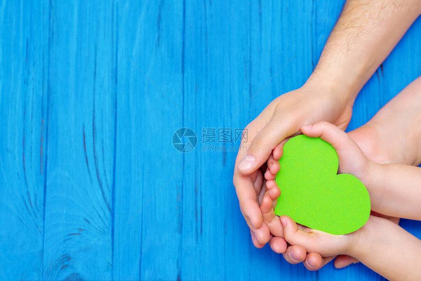 木制蓝色背景的成人和儿童手中的绿色心脏的顶部视图世界环境日世界卫生日和日的概图片