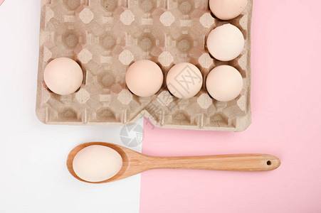木勺上的鸡蛋白色和粉红色背景上的一盘鸡蛋带睾丸的生态托盘简约趋势图片