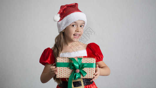 一个穿着圣诞服装的小女孩的肖像礼物在浅色上图片