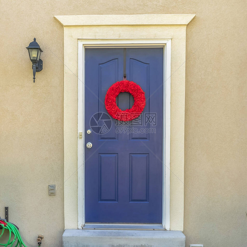 方形框架通往带有红色花环的家蓝色木制前门的混凝土台阶这座住宅的院子里种着图片