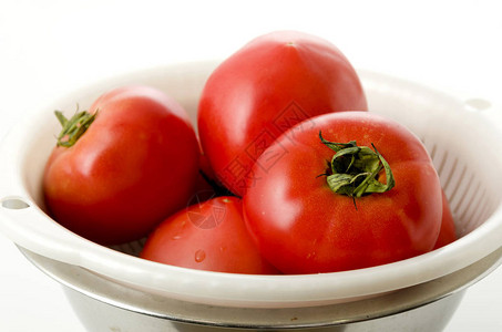 白色背景不锈钢碗滤锅中熟红番茄图片