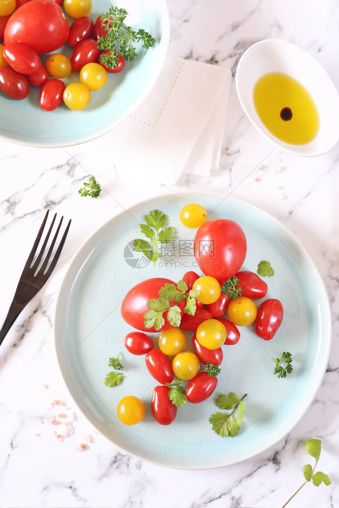 蓝盘上的各种红黄樱桃番茄浅色背景中的香菜和橄图片
