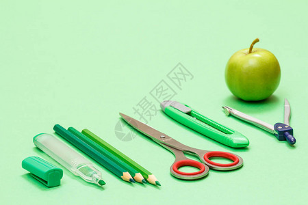 学校用品毡笔彩色铅笔剪刀裁纸刀指南针和绿色背景上的苹果回到学校的图片