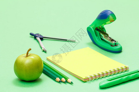 苹果彩色铅笔指南针笔记本裁纸刀和绿色背景上的订书机回到学校的概念学校图片