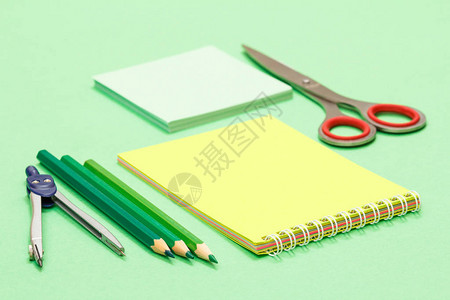 指南针彩色铅笔记本便条纸和绿色背景上的剪刀回到学校的概图片