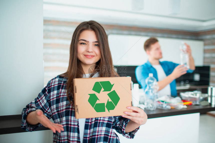 年轻的家庭在厨房里对材料进行分类以进行回收可回收材料必须分开妻子拿着一个带有绿色回收标志的纸板箱丈夫在图片