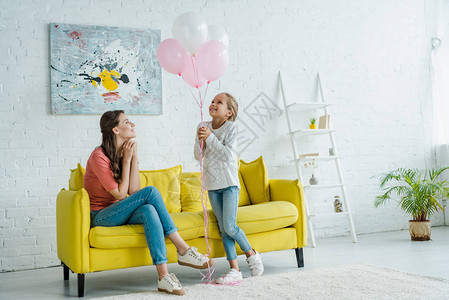 坐在沙发上看着快乐的孩子身边的粉色气球图片