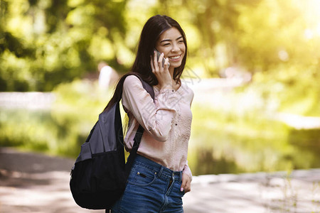 快乐的韩国女孩与背包聊天在移动电话室外交谈图片