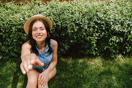 坐在灌木丛旁的伸手的草帽上快乐女孩有选择图片