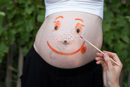 在孕妇笑脸的肚子上手拿刷子画图片