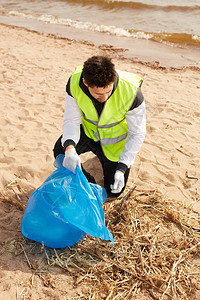 年轻的当代志愿者穿着制服在沙滩上捡垃圾图片