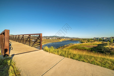 有金属护栏的桥梁环绕着一个反映清蓝天空的湖泊草原房屋和山岳也可以从这图片