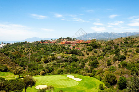 一座高尔夫球场对着一座山丘一个隐蔽的现代村庄山峰和蓝天图片